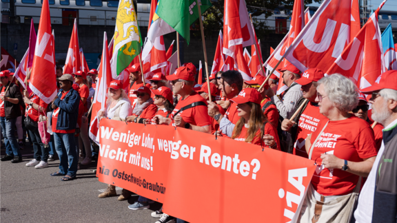Menschen in roten Unia-Shirts demonstrieren mit Fahnen und Transparenten für bessere Löhne und Renten.